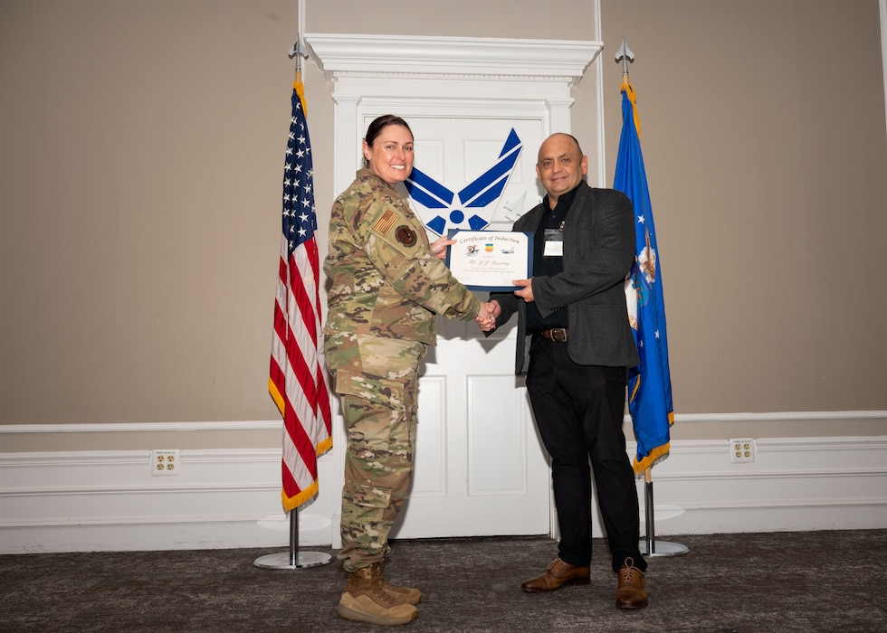 Service member and Honorary Commander shake hands while holding a certificate.