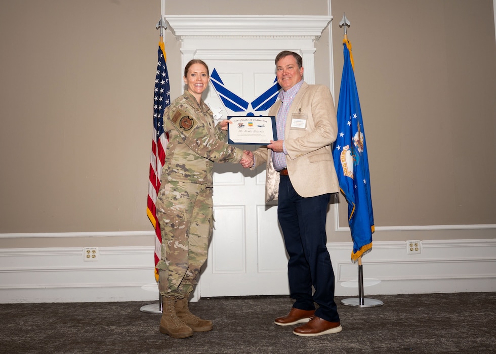 Service member and Honorary Commander shake hands while holding a certificate.