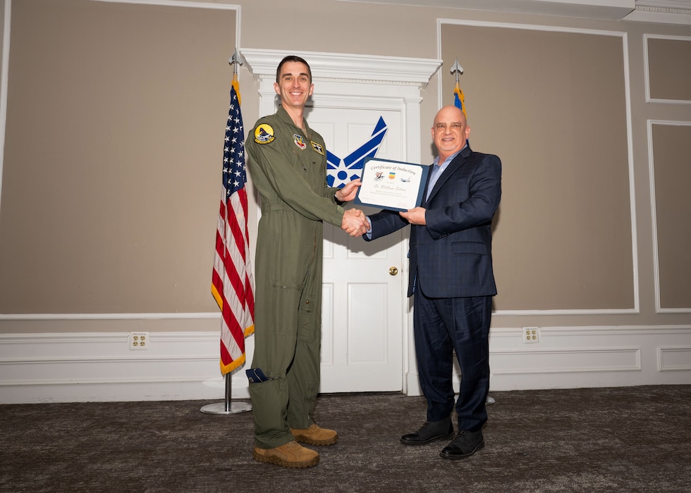 Service member and Honorary Commander shake hands while holding a certificate.