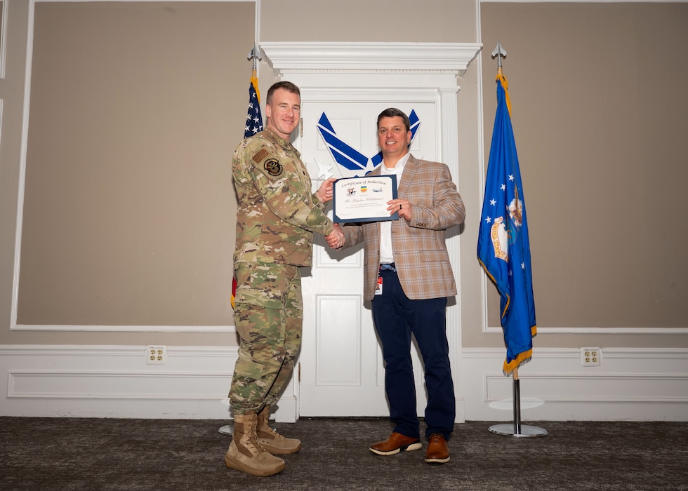 Service member and Honorary Commander shake hands while holding a certificate.