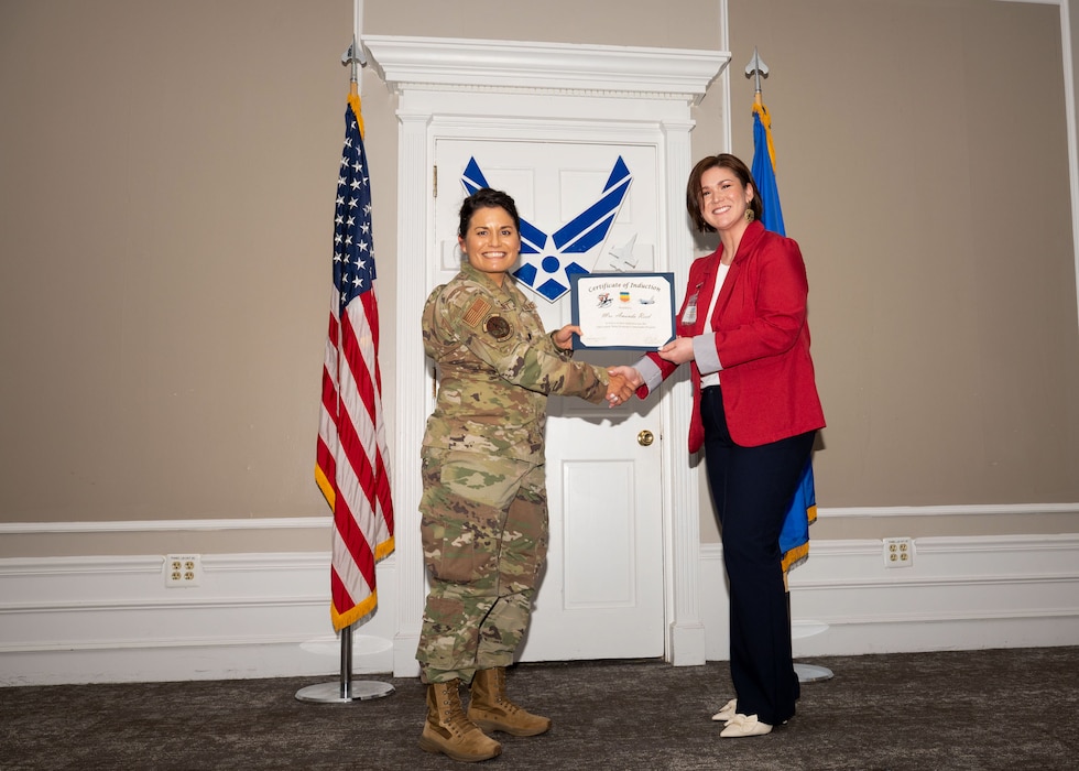 Service member and Honorary Commander shake hands while holding a certificate.