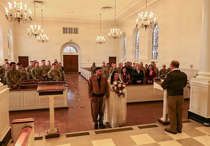 U.S. Army Spc. Ester Henriquez, an Indiana National Guard member assigned to Joint Task Force - District of Columbia, holds Hasan Alpkan's hand during their wedding ceremony at the Old Post Chapel on Fort Myer, Virginia, March 21, 2026. About 2,700 National Guard members support the D.C. Safe and Beautiful mission, assisting the Metropolitan Police Department in maintaining public safety for residents, commuters and visitors throughout the District.