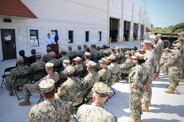 Military personnel listen to a man speak at a podium.