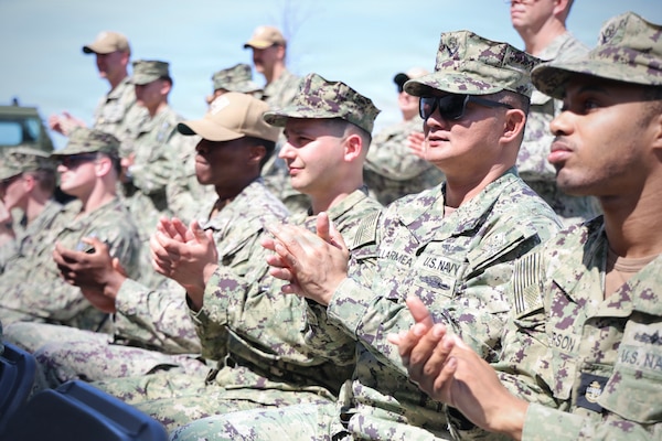 Sailors in uniform sit and applaud.