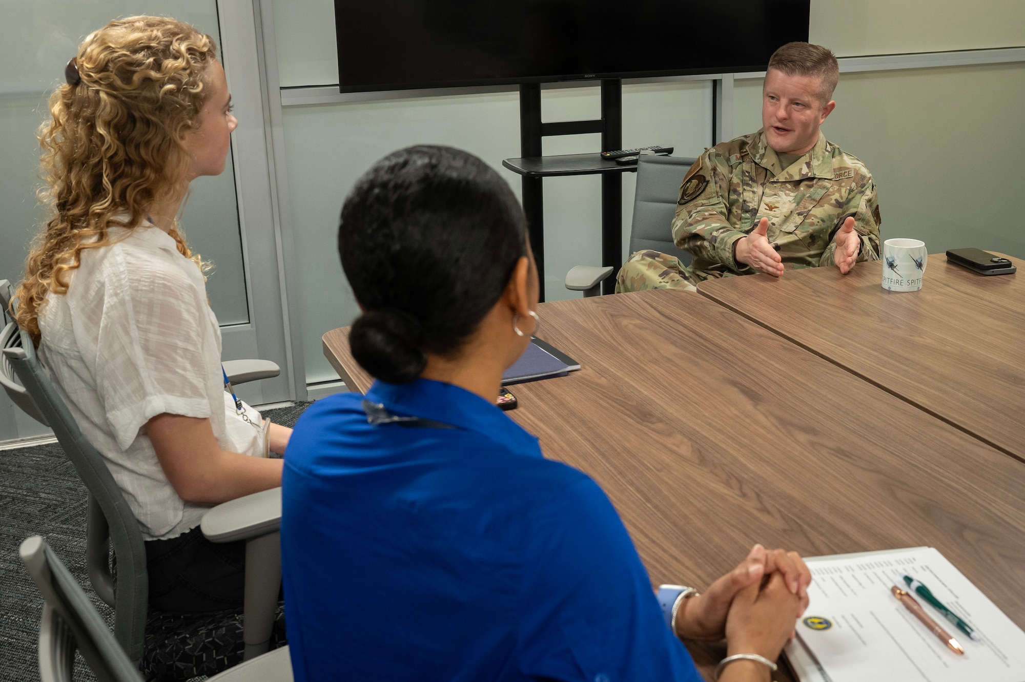 Two women sit facing a man in a US Air Force uniform. They are all talking.