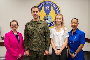 Three women and one man wearing a Polish military uniform stand in front of a sign that says AFSAC.