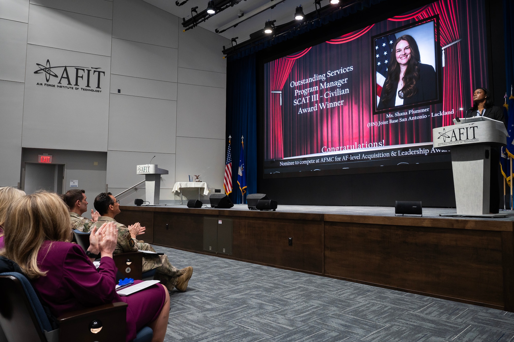 Image shows a woman on screen as winner of a civilian acquisition award.