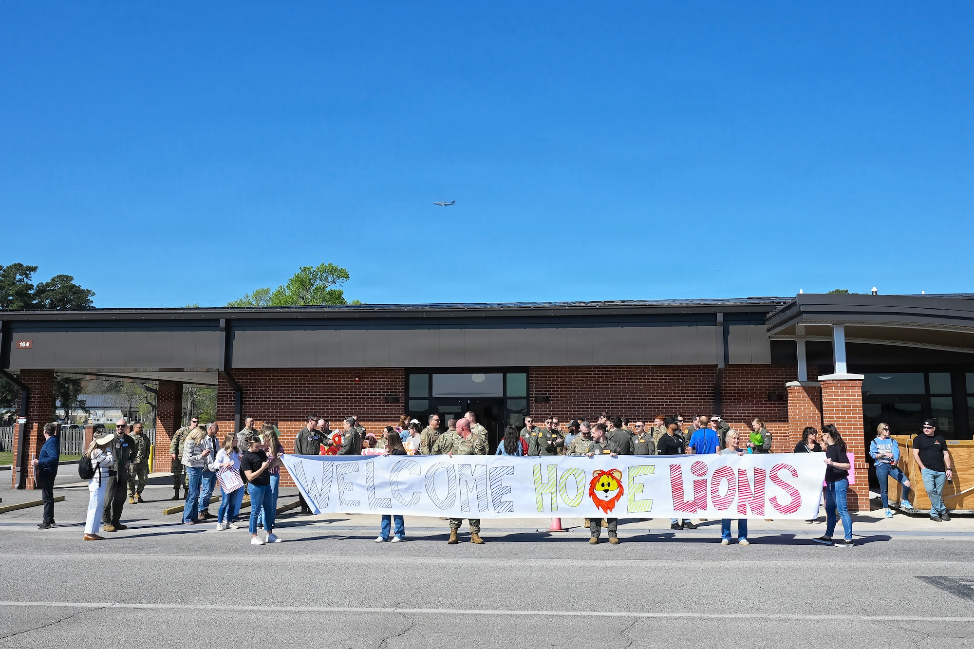 Airmen and family members hold a sign that says, "welcome home lions."