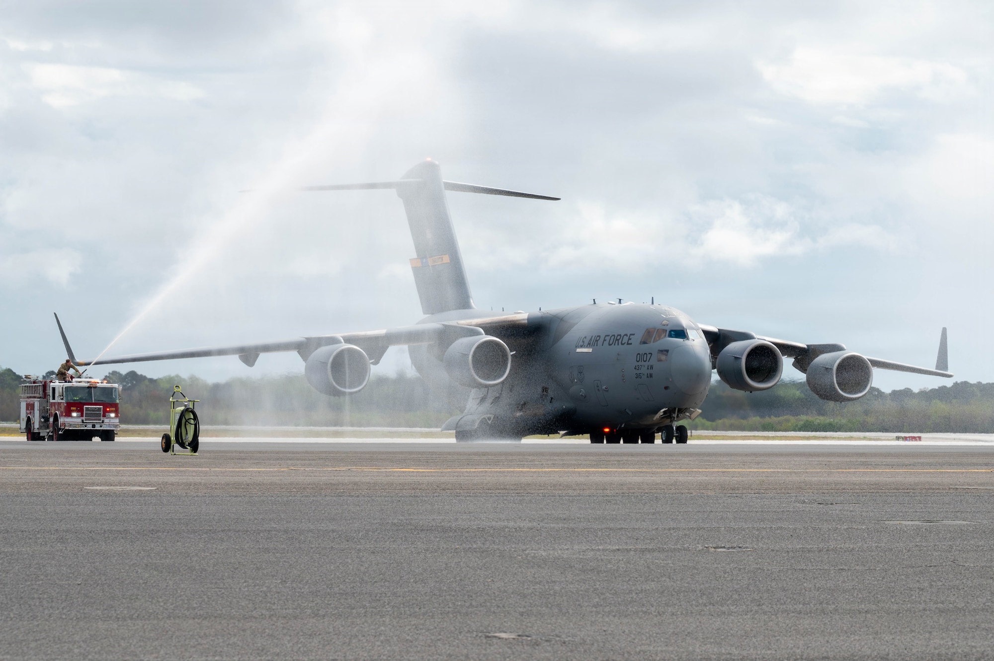 A C-17 Globemaster III aircraft is sprayed by two firetrucks on either side of it on the flightline.