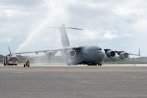 A C-17 Globemaster III aircraft is sprayed by two firetrucks on either side of it on the flightline.