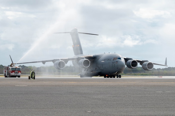 A C-17 Globemaster III aircraft is sprayed by two firetrucks on either side of it on the flightline.