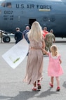 A woman and young girl walk toward a C-17 Globemaster III aircraft holding a sign that reads "welcome home."