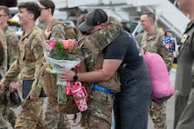 An Airman and a Civilian embrace, the civilian is holding a bouquet of flowers.