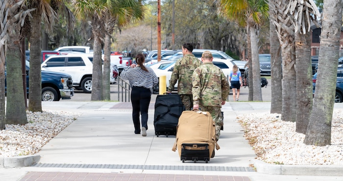 Airmen and civilians walk with their backs to the camera, pulling large bags behind them.