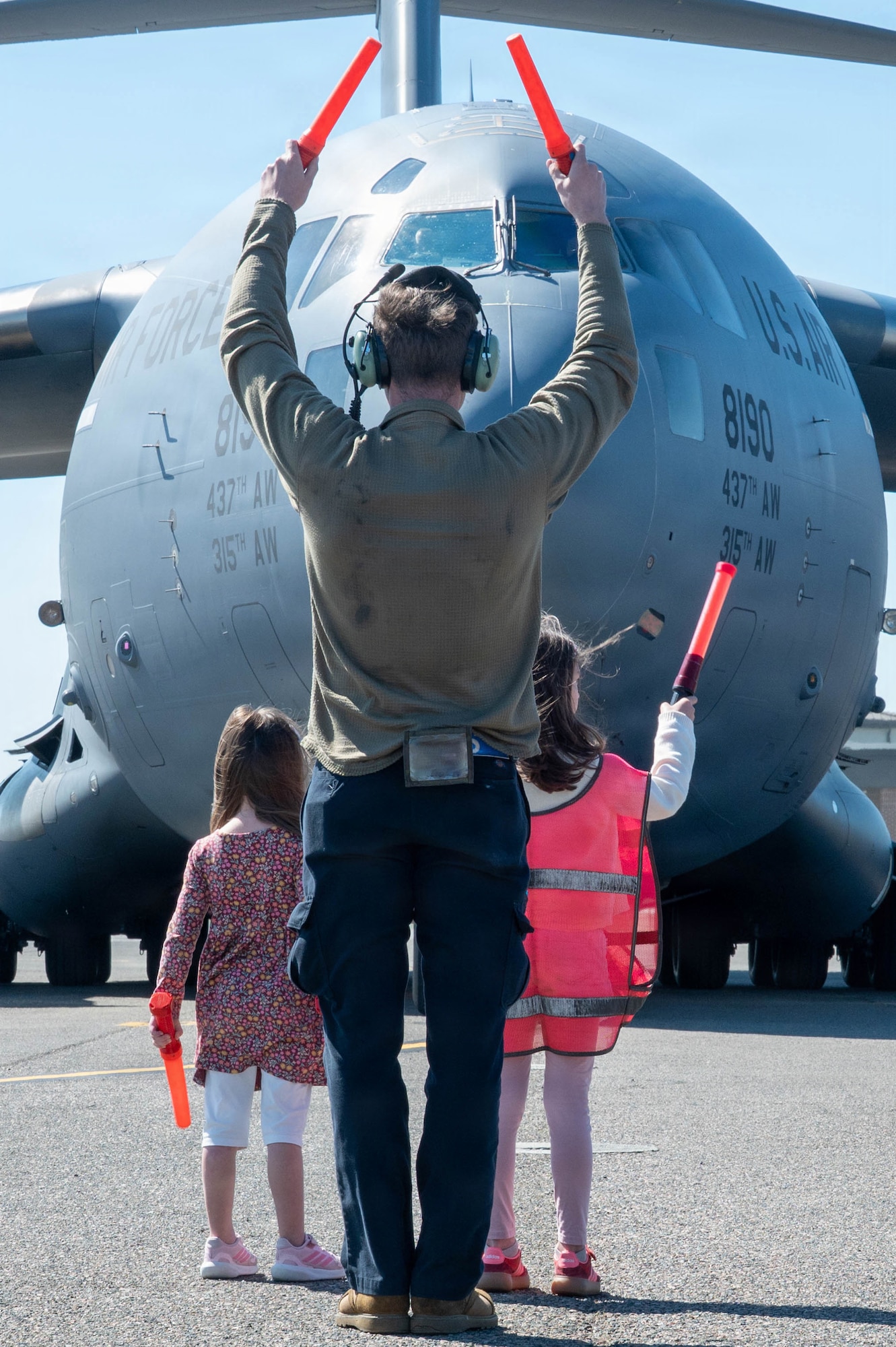 A man and two young girls air marshal in a C-17 Globemaster III aircraft on a flightline.