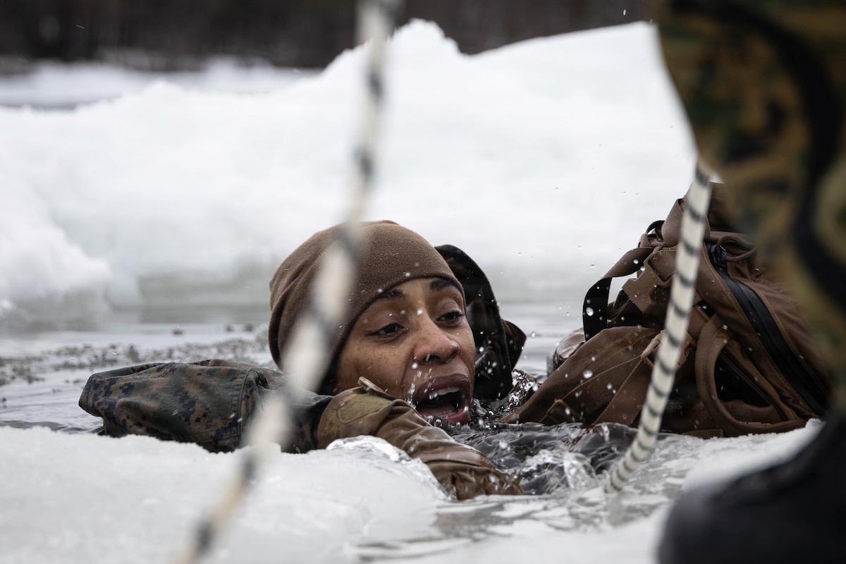 A sailor takes a breath while attempting to climb out of freezing waters surrounded by snow as seen through a net.