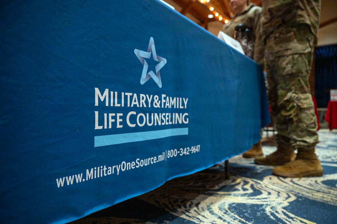 A service member, visible from the legs down, stands at a booth that says "Military & Family Life Counseling."