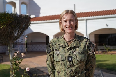 Female service member stands in the courtyard of a white building