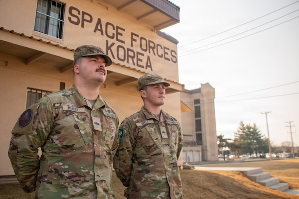 U.S. Space Force Spc. 4 Ethan Mansel, left, and Spc. 4 Brandon Spitz, both attached to U.S. Space Forces – Korea during exercise Freedom Shield 26, pose in front of the unit headquarters at Osan Air Base, Republic of Korea, March 17, 202