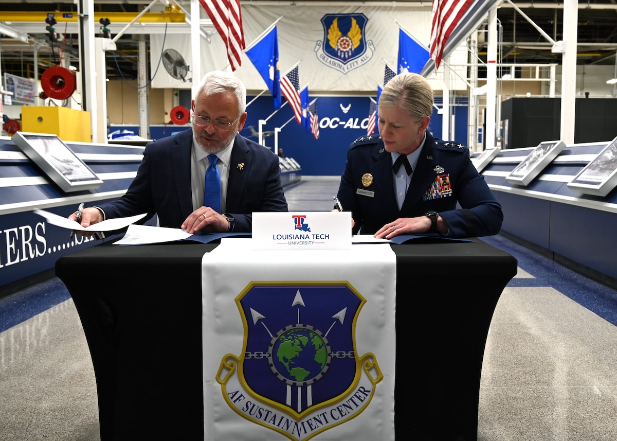 A civilian and military leader signing an agreement.