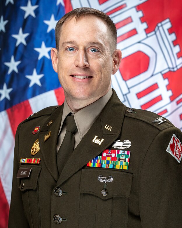 U.S. Army Col. Eli S. Adams in his Army Green Service Uniform in front of a U.S. flag and the U.S. Army Corps of Engineers flag.