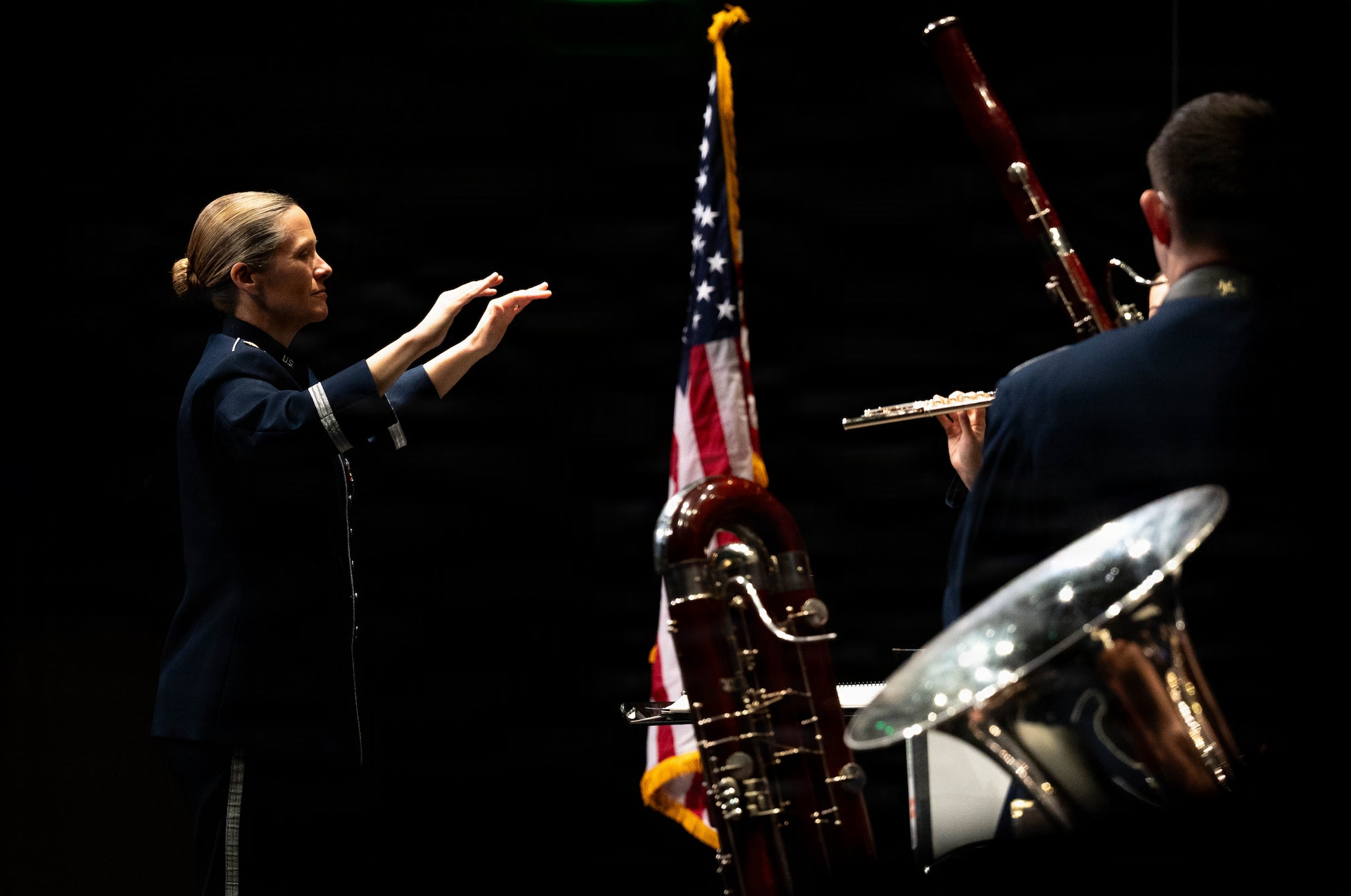 An Airman conducts a band, dramatically lit, on a stage.