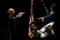 An Airman conducts a band, dramatically lit, on a stage.