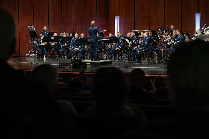A band performs on a lit stage while audience members watch in the dark.