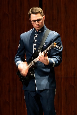 An Airman plays the electric guitar, the motion of his hand blurs.