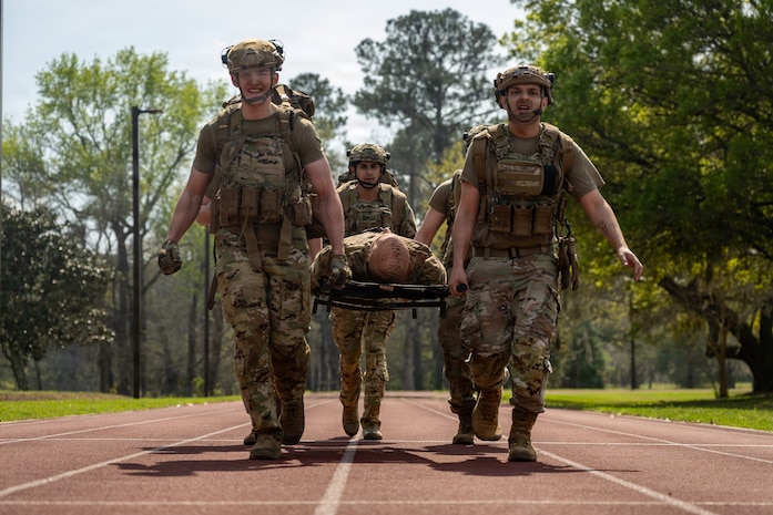 Airmen carry a mannequin on a stretcher over a track.