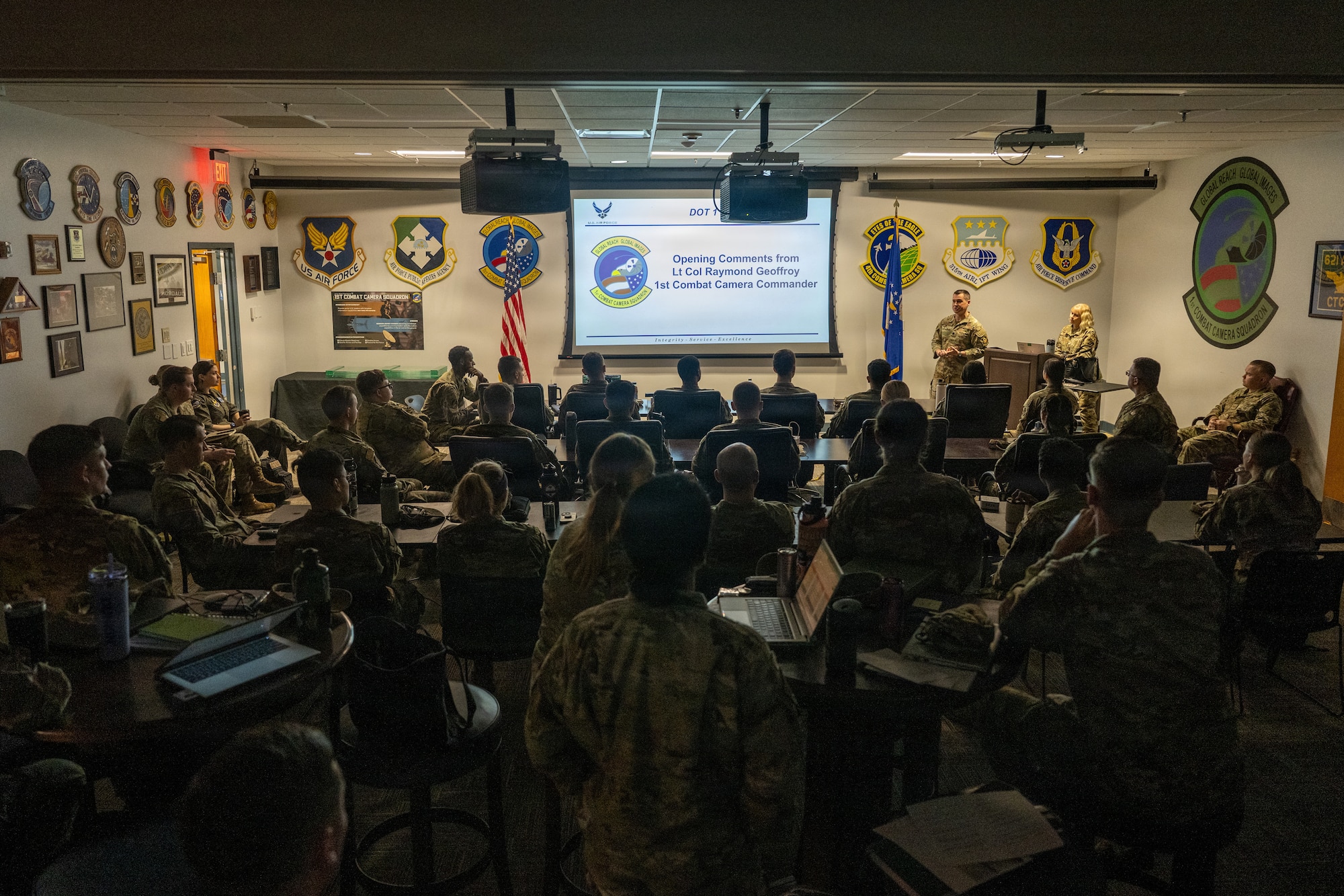 Airmen sit in a room receiving opening comments from leadership.