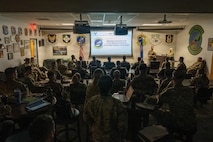 Airmen sit in a room receiving opening comments from leadership.