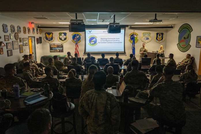 Airmen sit in a room receiving opening comments from leadership.