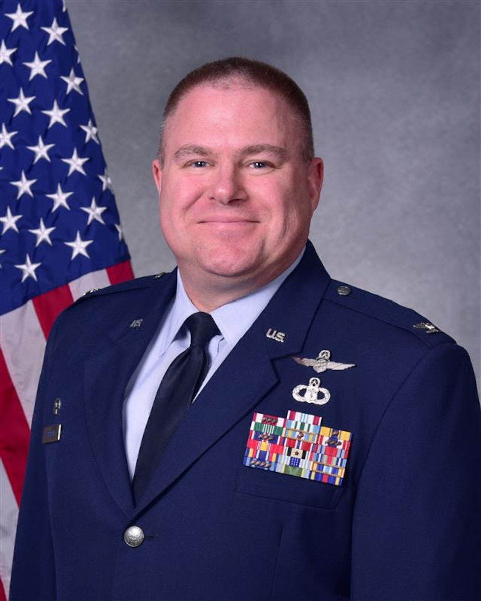 Man in uniform poses for photo in front of flag