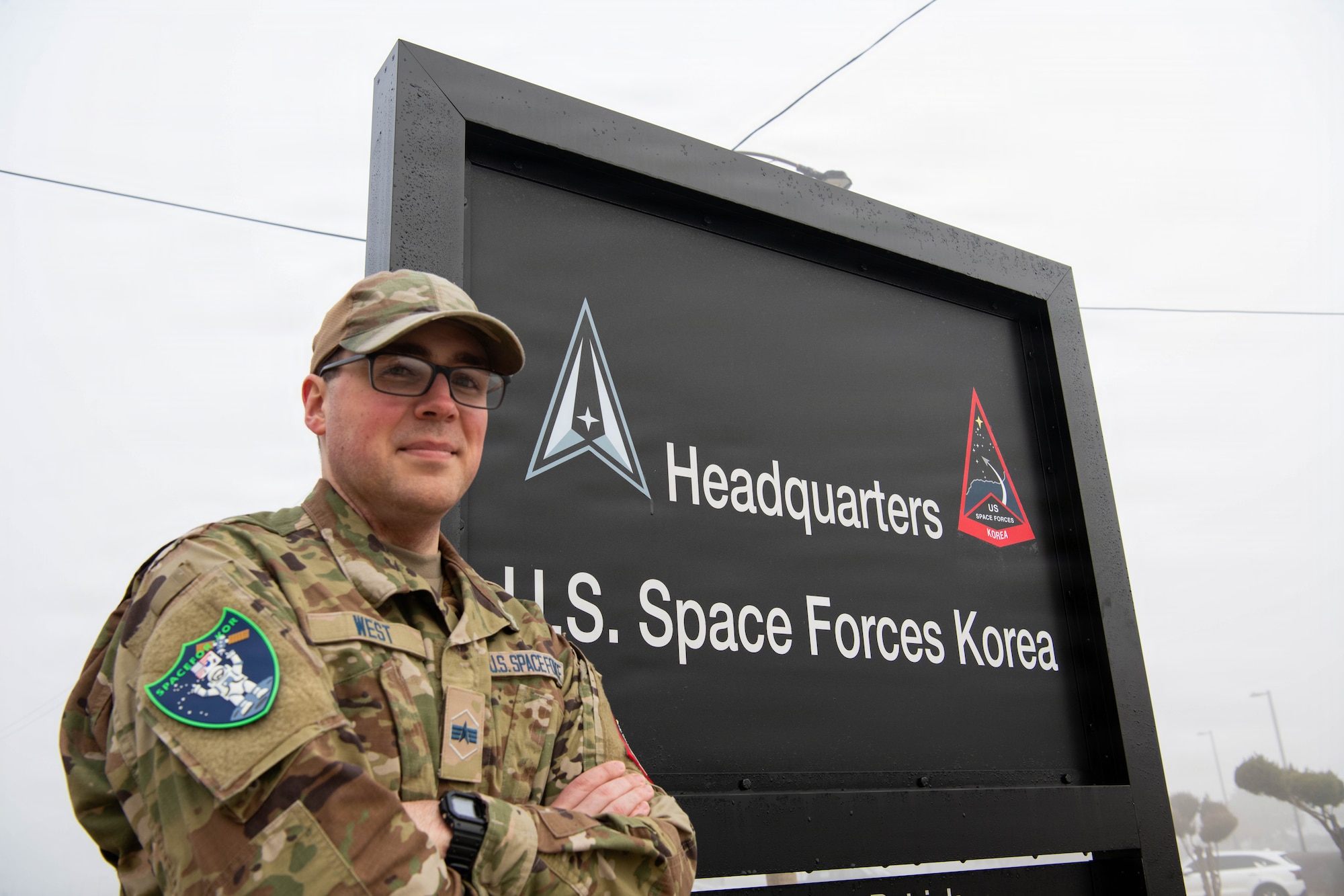 U.S. Space Force Spc. 4 Bradley West, a wideband transmissions controller assigned to USSF Combat Forces Command's Mission Delta 8, 53rd Space Operations Squadron, Detachment 2, poses for a photo in front of a U.S. Space Forces - Korea sign during exercise Freedom Shield 26 at Osan Air Base, Republic of Korea, March 12, 2026. West served as a non-kinetic effects duty officer during FS26, coordinating simulated space operations capabilities for U.S.-ROK forces. (U.S. Space Force photo by 2nd Lt. Andrew Taller)