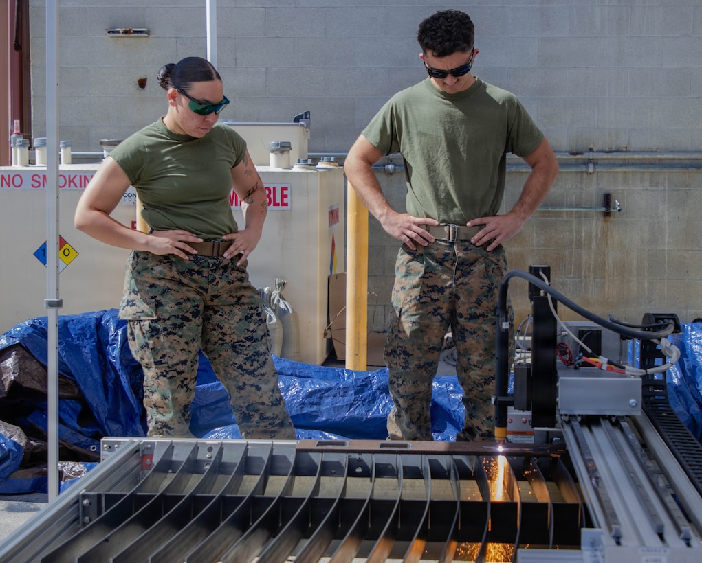 Two Marines watching a piece of metal being cut