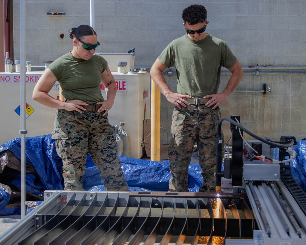 Two Marines watching a piece of metal being cut