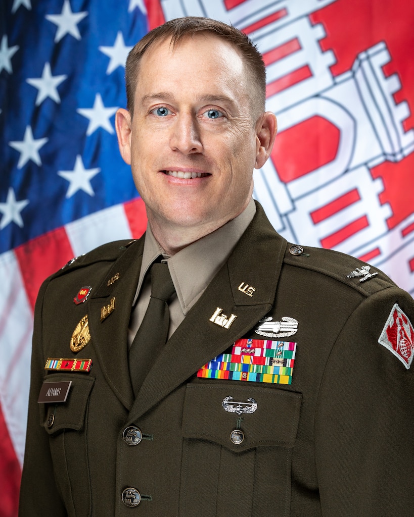U.S. Army Col. Eli S. Adams in his Army Green Service Uniform in front of a U.S. flag and the U.S. Army Corps of Engineers flag.