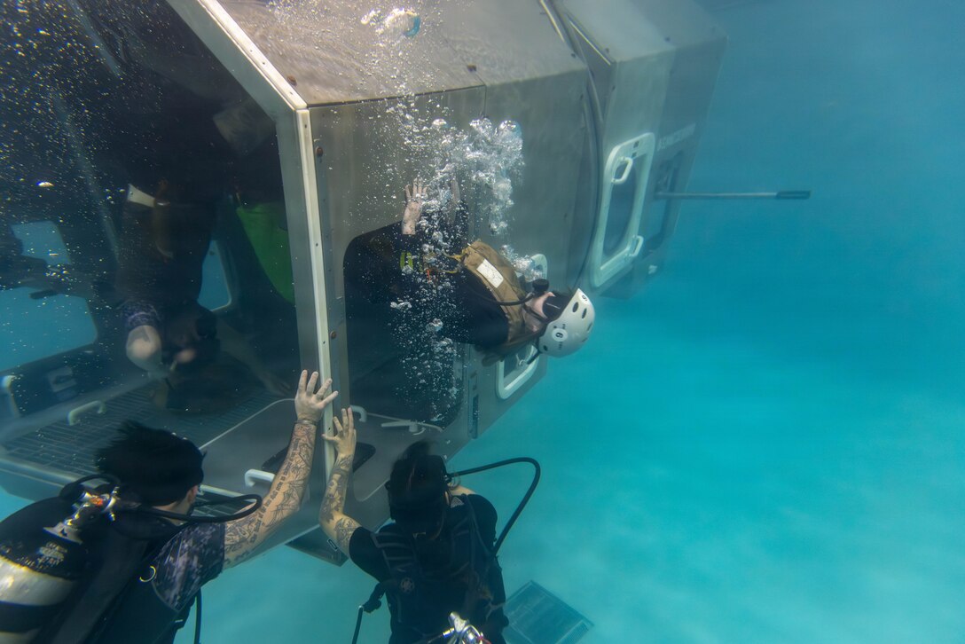 U.S. Marine Corps Lance Cpl. Sabine Wilson, a combat photographer with II Marine Expeditionary Force Support Battalion pushes herself out of a modular amphibious egress trainer (MAET) during an underwater egress training at Marine Corps Base Camp Lejeune, North Carolina, March 24, 2026. UET provides Marines and Sailors with the skills and confidence to safely evacuate an aircraft submerged in water. (U.S. Marine Corps photo by Lance Cpl. Channah Chilton.)