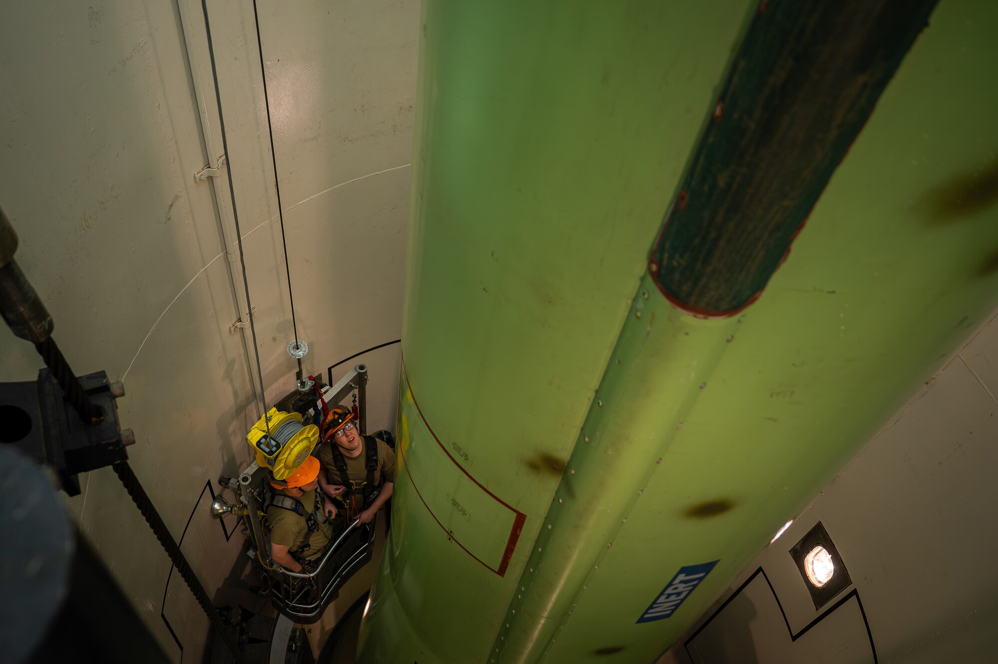 Two uniformed men works in a missile silo trainer.