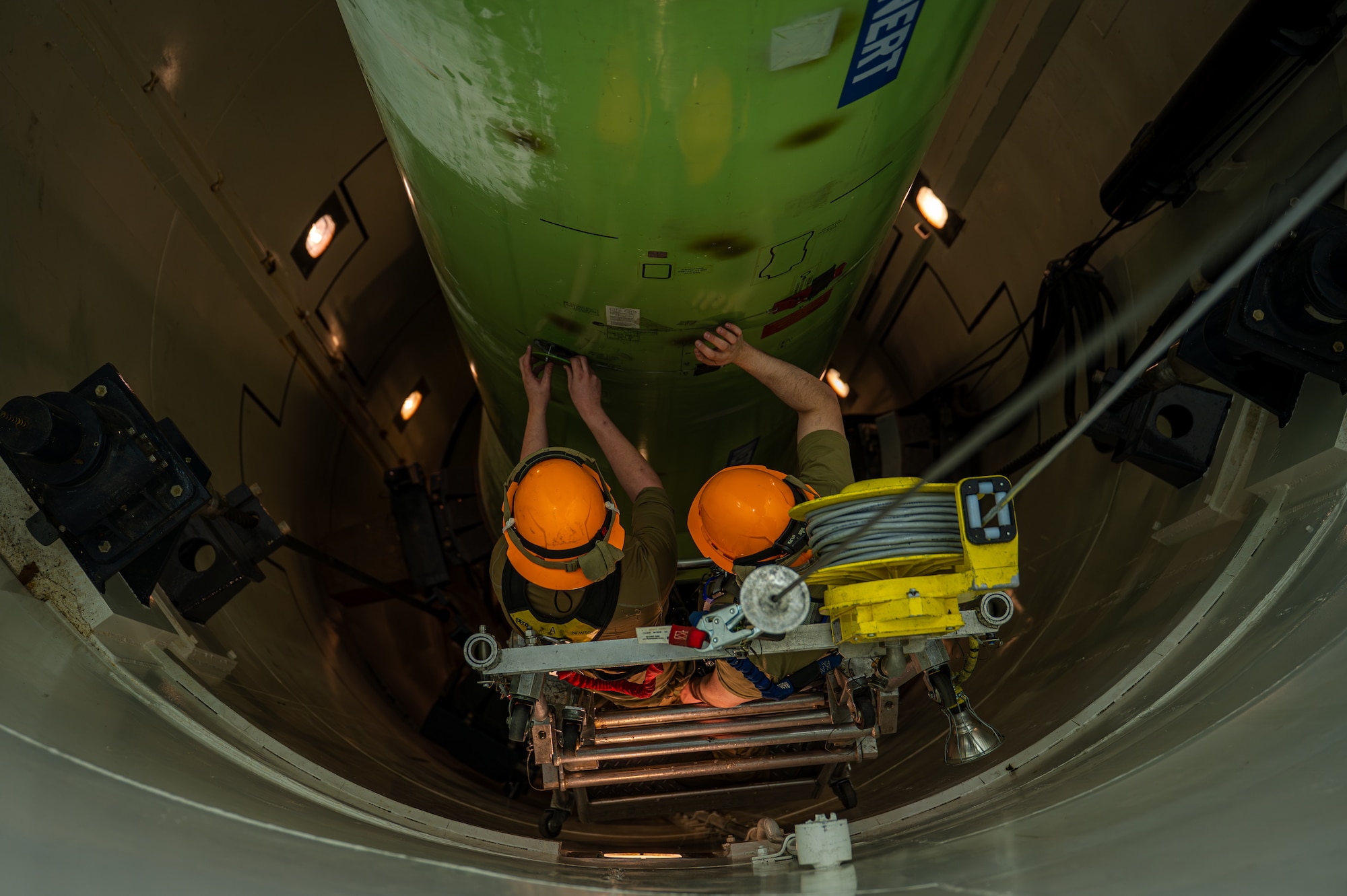 Two men in uniform works on a trainer missile.