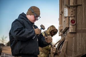 A uniformed man uses a hammer.