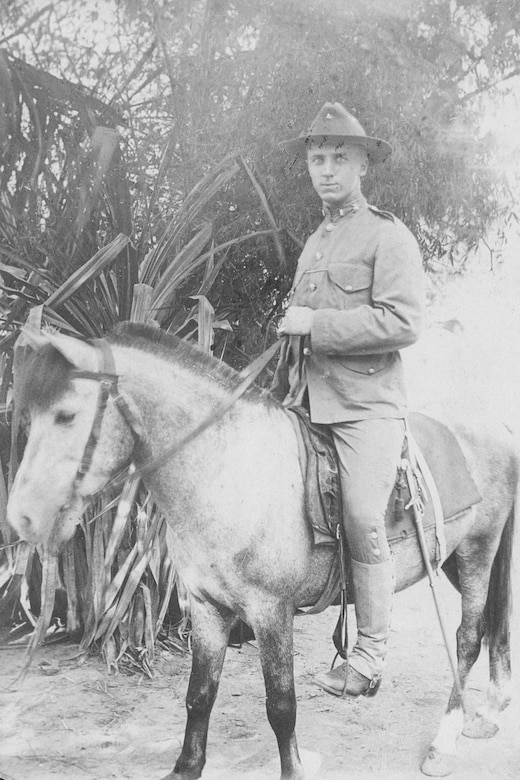 A man wearing a military uniform poses for a photo while sitting on a horse and holding its reins.