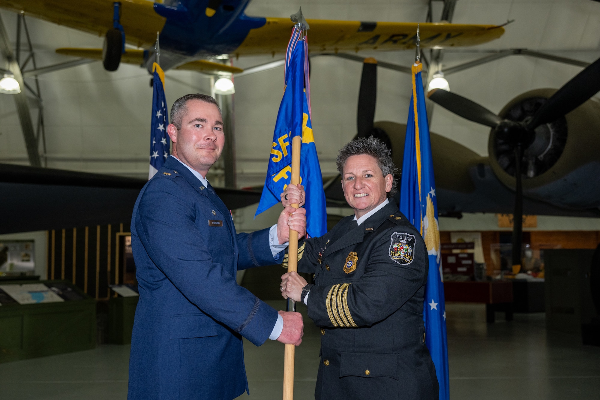U.S. Air Force Maj. Daniel Parsons, 436th Security Forces Squadron commander, left, and Chief Celia Ashe, Milford Police Department Chief of Police, pose holding the 436th SFS guidon at the Class of 2026 Honorary Commanders Induction Ceremony at the Air Mobility Command Museum, Dover Air Force Base, Delaware, March 24, 2026. The passing of the guidon is a military tradition welcoming a new commander to the unit. (U.S. Air Force photo by Mauricio Campino)