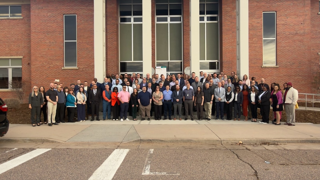 A large group of people pose for a photo in front of a brick building.