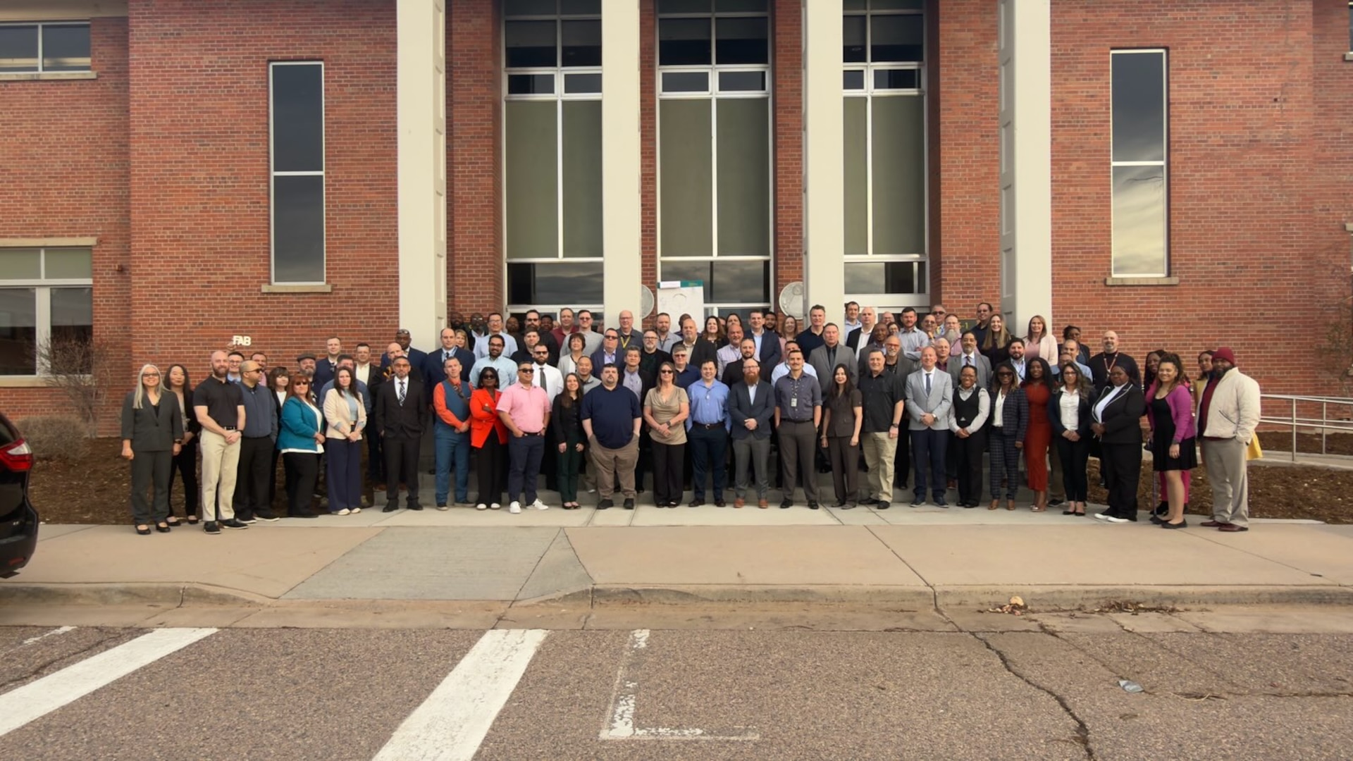 A large group of people pose for a photo in front of a brick building.