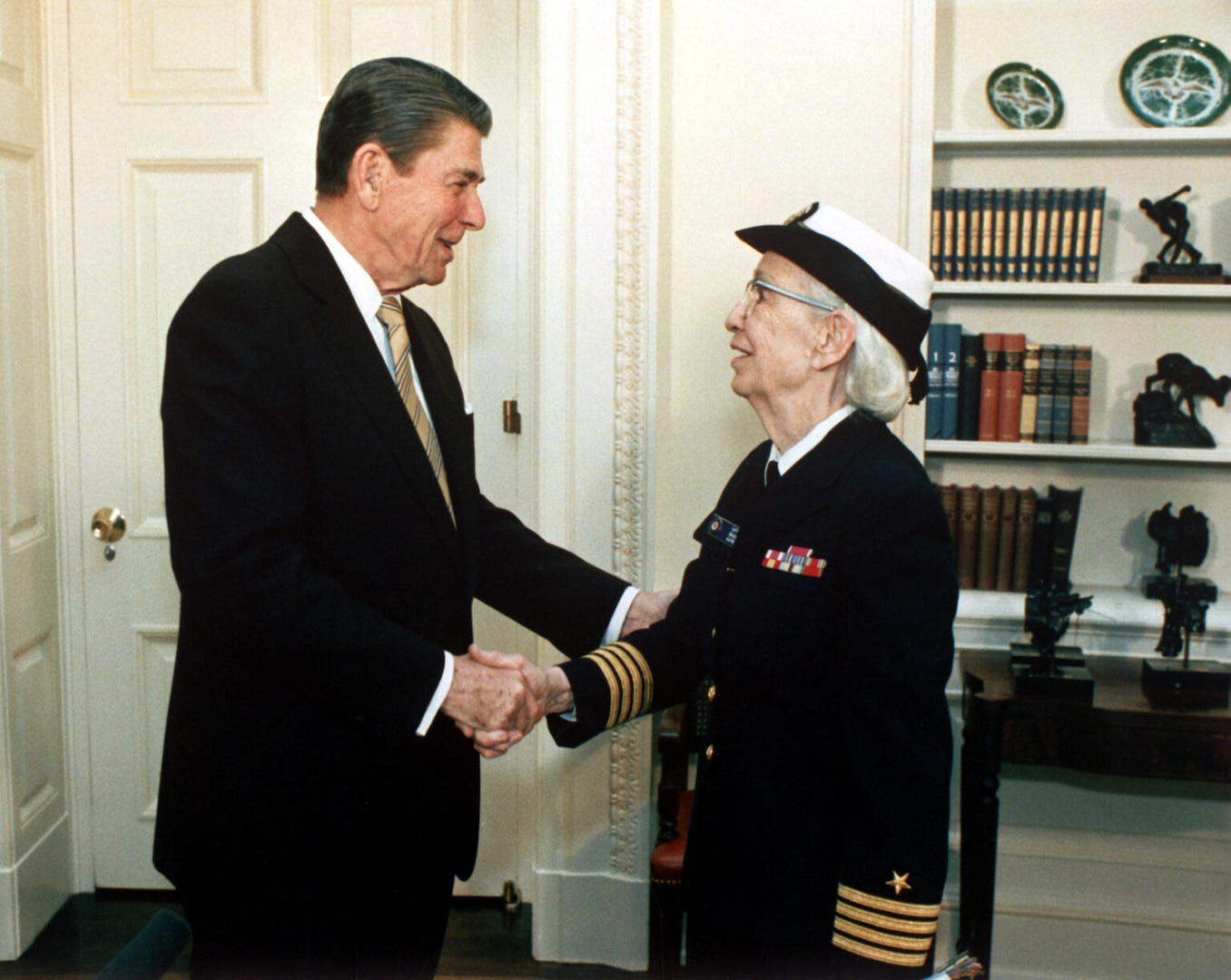 On Dec. 15, 1983, at the White House, President Ronald Reagan congratulates Grace Hopper on her promotion from Captain to Commodore, a title later redesignated as Rear Admiral (Lower Half). Hopper’s decades of service helped shape the Navy’s transition toward standardized, enterprise-scale computing systems. (Photo by Pete Souza, Department of Defense)