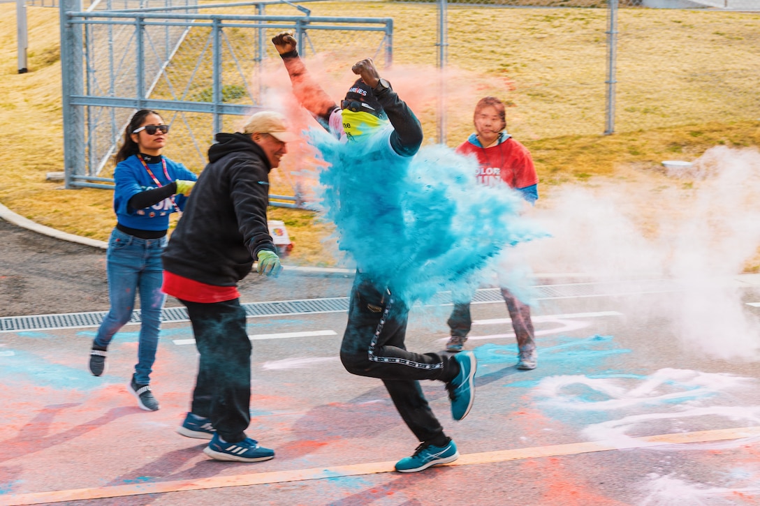 Volunteers from Marine Corps Air Station Iwakuni throw colored corn starch on a participant of a Marine Corps Total Fitness color run, at MCAS Iwakuni, March 7, 2026. Marine Corps Community Services Iwakuni’s Semper Fit program and Naval Family Branch Clinic Iwakuni’s Joint Behavioral Health program worked hand and hand to organize the color run, increasing awareness about programs on base that will help support mission readiness and overall well-being for service members and their families.(U.S. Marine Corps photo by Cpl. Sarah Grawcock)