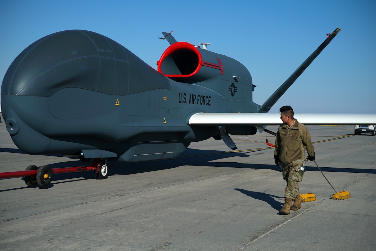 Photo shows an Airman carrying chocks in front of an aircraft on the flight line