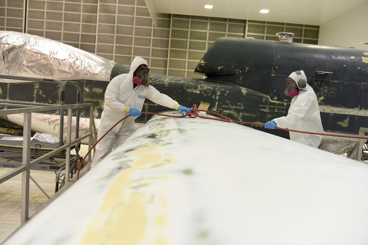 photo shows a paint stripped aircraft and two individuals sanding its wing